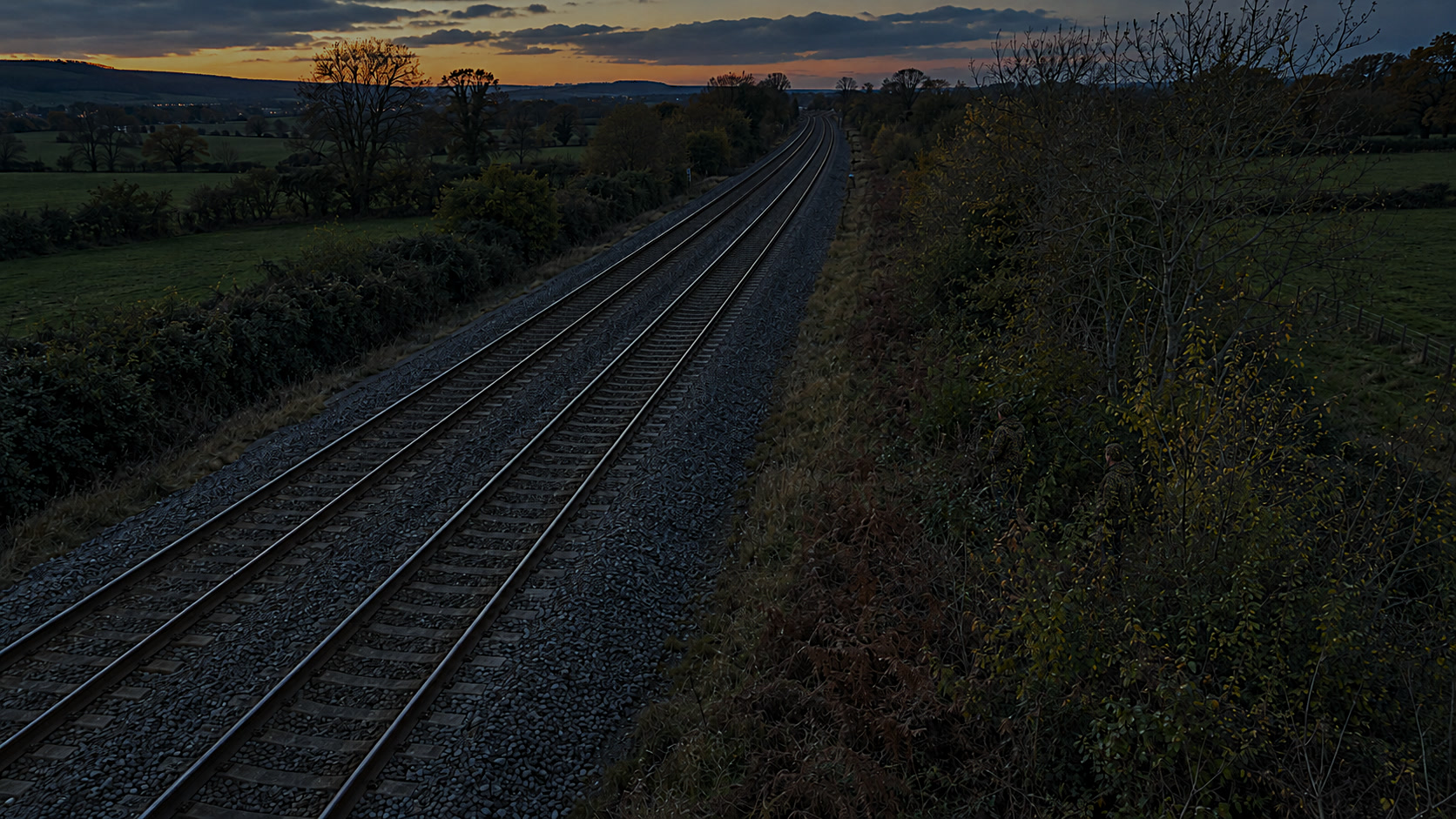 Illustrative railway scene at dusk, with two people beside the tracks on the right